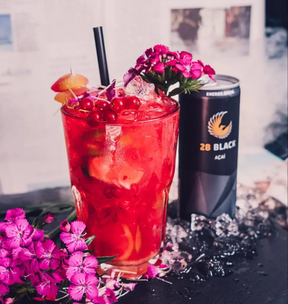 Roter Cocktail mit Blüten und Eiswürfeln